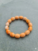 Natural orange marble-pattern beaded stretch bracelet displayed in a circular shape on a textured grey stone background.