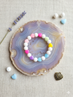 Cute colorful heart bead bracelet with pastel pink, blue, yellow, green, and purple heart-shaped beads displayed inside a transparent jewelry display box on a wooden surface with decorative flowers and accessories.