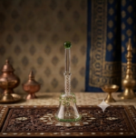 Clear glass pooja bell with green Om symbols displayed in a serene garden setting with fresh floral garland and natural sunlight.